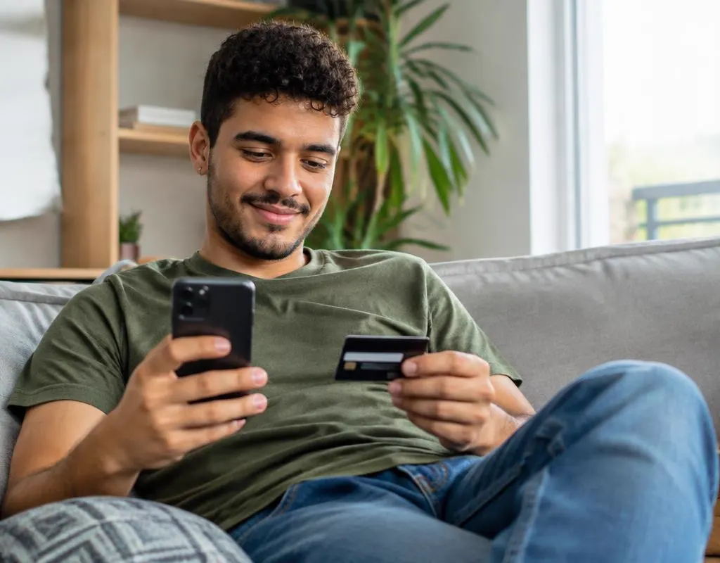 Homem no sofá conferindo o celular antes de pagar com cartão
